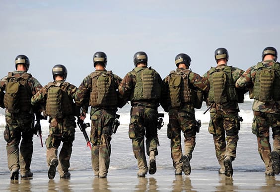 A group of soldiers walking across the beach.